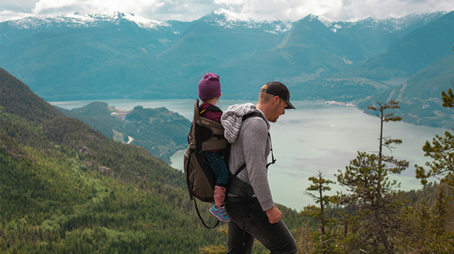 Father walking through mountainous landscape with a child on his back